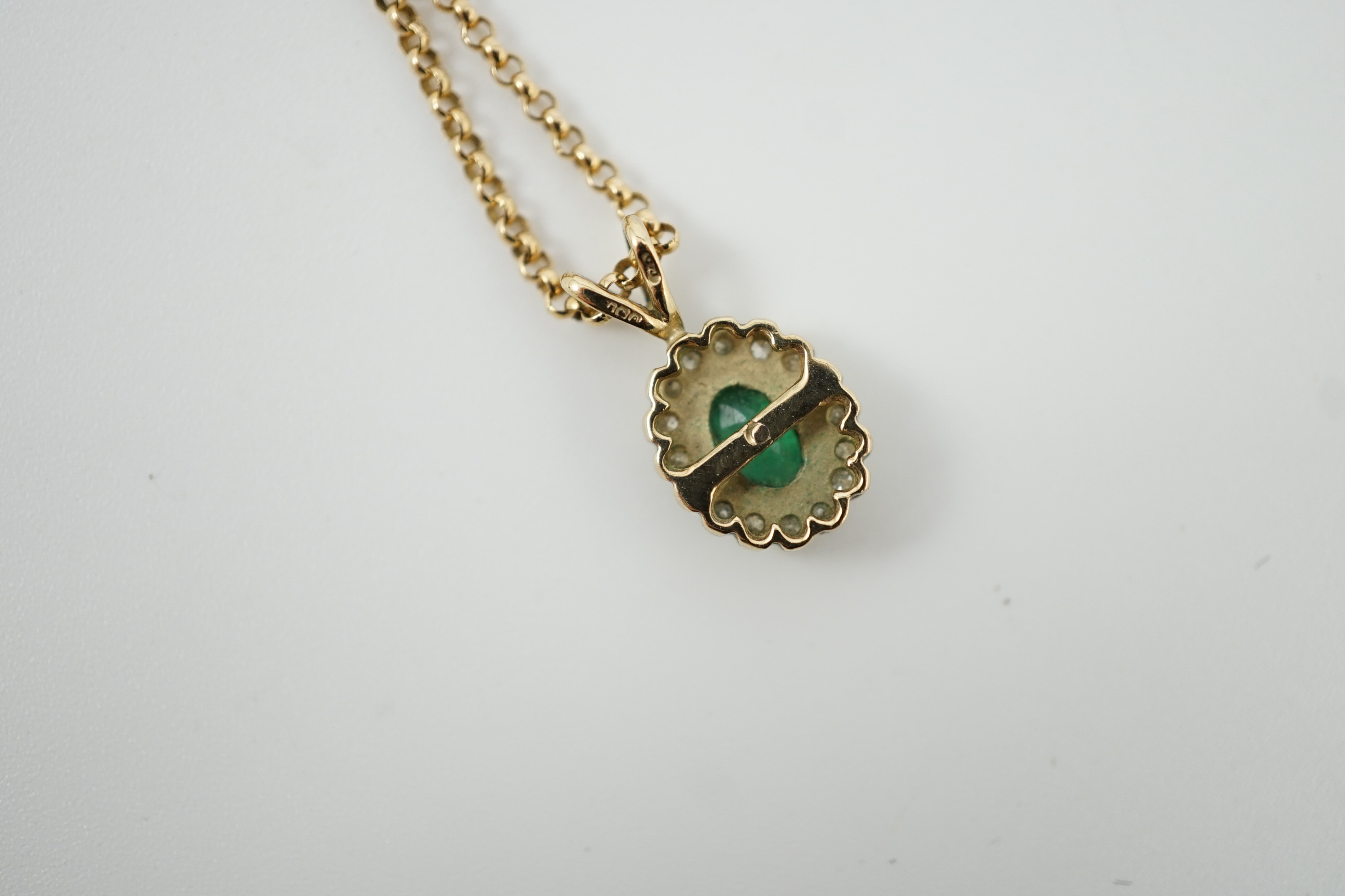 A modern 9ct gold, emerald and diamond set oval cluster pendant, 16mm, on a 9ct gold chain, 44cm, gross weight 4.1 grams.